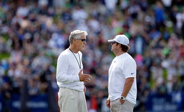 Seattle Seahawks head coach Pete Carroll, left, talks with general manager John Schneider as fans fill a hill behind at an NFL football camp practice Friday, July 25, 2014, in Renton, Wash.